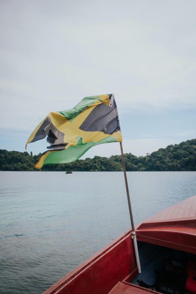 Jamaican flag waving majestically on a red boat against a serene lake backdrop.